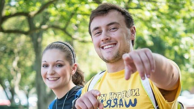 Male student pointing at the photographer while walking with a female classmate